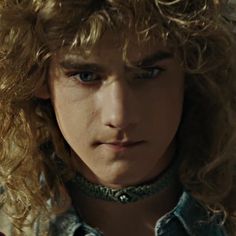 a close up of a person with curly hair and blue eyes wearing a collared shirt