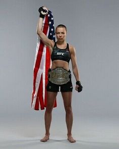 a female fighter holding an american flag and wearing a black top with her hands in the air