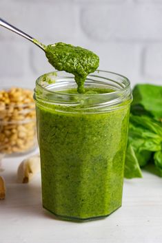 a jar filled with green pesto next to spinach leaves and other vegetables on a table