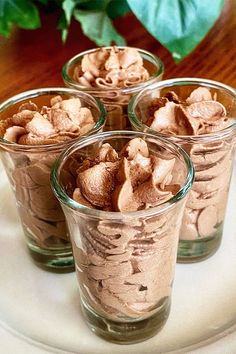 four glasses filled with dessert sitting on top of a white plate