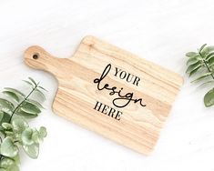 a wooden cutting board with the words your design here on it next to some plants