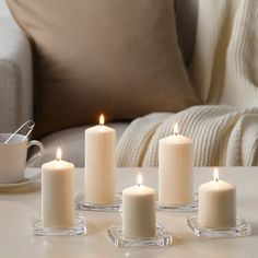 five white candles sitting on top of a table next to a cup and saucer