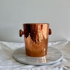 a copper colored cup sitting on top of a white marble plate with a wooden handle