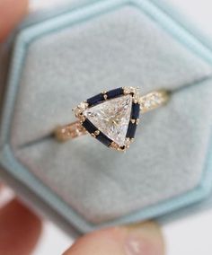 someone is holding an engagement ring with a triangle shaped diamond and blue sapphire stones on it