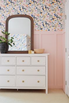 a white dresser sitting in front of a pink wall with a mirror on top of it