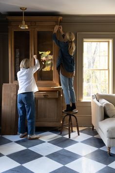 two children are painting the wall in their living room with checkered flooring and furniture