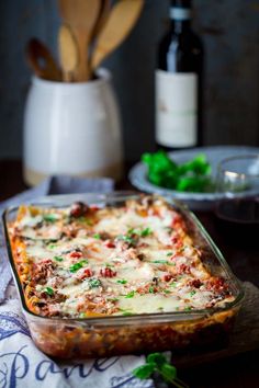 a casserole dish with meat, cheese and vegetables in it next to a bottle of wine