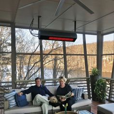 two people sitting on a couch with a dog in front of them, looking out the window