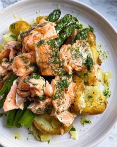 a white plate topped with salmon, potatoes and asparagus covered in seasoning