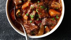 a white bowl filled with beef stew and carrots on top of a black table