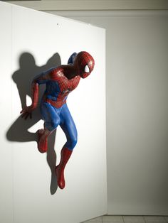 a statue of spider - man hanging from the side of a white wall in a room