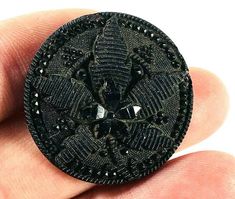 a hand holding a small black brooch in it's right hand, with an intricate design on the center