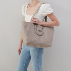 This bag has everything you want in a tote top zip closure, a padded tech pocket, solid leather straps, and Sheilas signature circular handles that fold down when not in use Sheila EastWest Tote in Pebbled Leather  Taupe Tote Bag in Taupe | Hobo® Modern Soft Leather Satchel For On-the-go, Versatile Hobo Bag With Round Handle For Daily Use, Versatile Satchel With Round Handle For On-the-go, Leather Satchel With Round Handle For Everyday Use, Travel Shoulder Bag With Soft Leather And Round Handle, Leather Bag With Round Handle For Everyday Use, Everyday Double Handle Weekender Bag, Beige Leather Weekender Bag With Handles, Beige Leather Weekender Bag