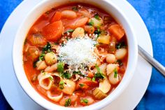 a bowl of pasta and vegetable soup with parmesan cheese on top, ready to be eaten