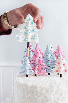 someone is decorating a cake with small trees on the frosting and sprinkles