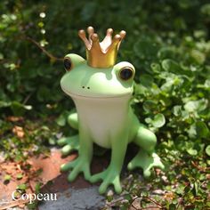 a green frog with a gold crown on it's head sitting in the grass