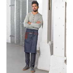 a man standing in front of a white wall wearing an apron and looking at the camera