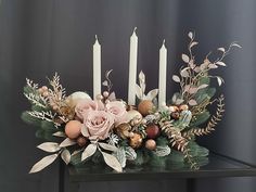 an arrangement of flowers and candles on a black table with grey walls in the background