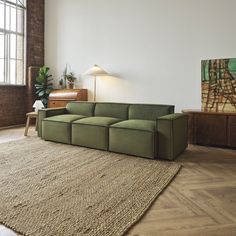 a green couch sitting on top of a wooden floor next to a large window in a living room