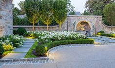 an outdoor garden with white flowers and greenery in the evening sun, surrounded by stone archways