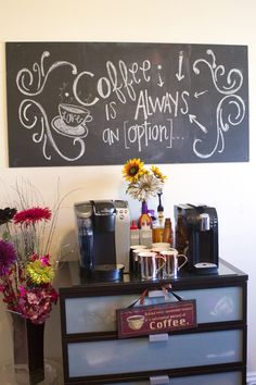 coffee is always on display in front of a chalkboard sign with flowers next to it