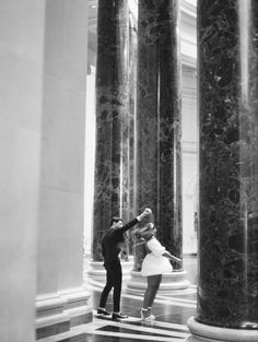 black and white photograph of two people dancing in the middle of an empty room with columns