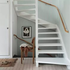 a white stair case next to a wooden chair in front of a painting on the wall