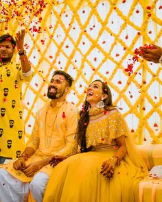 a man and woman sitting next to each other in front of a yellow backdrop with red confetti