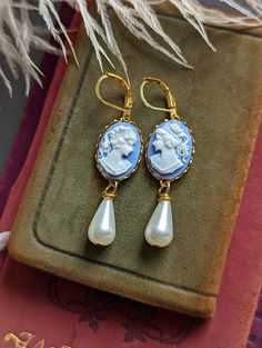 "Absolutely lovely, these peach cameo earrings are perfect for a Gothic or Historical period wedding! They would make an excellent gift for anyone that loves vintage-style jewelry. Featuring golden brass lace-edged bezel settings mounted with blue and white portrait cameos. Adorned with an elegant, teardrop shaped ivory glass pearl.  *Please note: the settings sometimes may have random designs on the back, this is common from processing and not noticeable while wearing. Size: Suspended by hook e Classic Cameo Earrings For Wedding, Elegant Cameo Clip-on Earrings Gift, Cameo Drop Earrings For Wedding, Cameo Drop Earrings For Formal Occasions, Elegant Cameo Earrings As Gift, Elegant Cameo Earrings For Gift, Elegant Cameo Earrings For Wedding, Cameo Drop Earrings Jewelry Gift, Classic Cameo Earrings