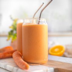 two glasses filled with carrot smoothie on top of a cutting board