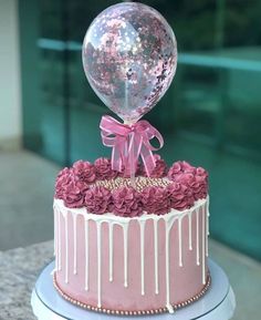 a pink cake with flowers and a balloon on top