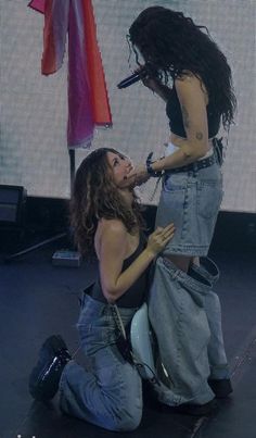 two women on stage with microphones in their hands and one woman kneeling down next to her