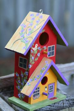 a colorful bird house sitting on top of a piece of wood