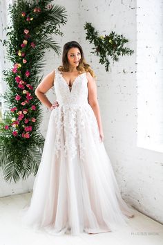 a woman in a wedding dress standing next to a floral arch with pink flowers on it