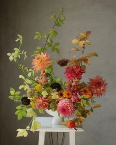 a vase filled with lots of colorful flowers on top of a white table next to a gray wall