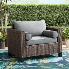 a wicker chair sitting on top of a blue and green rug next to a potted plant