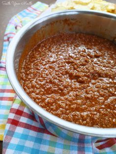 a bowl filled with chili on top of a checkered table cloth next to chips