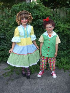 two young children dressed in colorful clothing standing next to each other near some bushes and trees