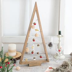 a wooden christmas tree with ornaments on it next to a candle and other holiday decorations