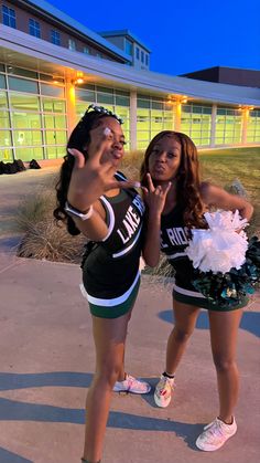 two young women dressed in cheerleader outfits giving the peace sign