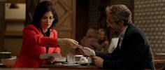 a man and woman sitting at a table in front of each other with coffee cups