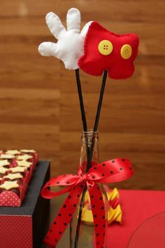 two red and white flowers in a vase with some cookies on the table behind it