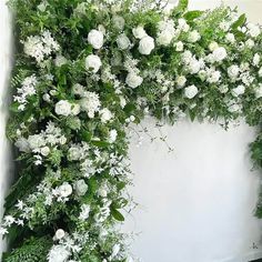 an arrangement of white flowers and greenery on a wall