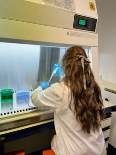 a woman in white lab coat and blue gloves working on a machine with green flasks