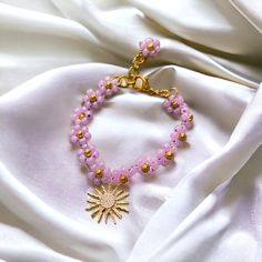 Rapunzel Sun Bracelet - Light Purple Glass Daisy Chain Flowers, 18K Gold-Plated Beads and Adjustable Chain, Perfect Gift for your Daughter, Sister, Girlfriend, Friend Add a dash of magic to your jewellery collection with the Rapunzel Sun Bracelet. This enchanting piece features a daisy chain design made of light purple glass flowers, each with a shimmering 18K gold-plated bead at the centre. The bracelet is finished with a Rapunzel-inspired sun charm, creating a whimsical, fantasy-inspired look Bohemian Gold Beaded Bracelet With Flower Charm, Handmade Gold Flower Charm Bracelet, Handmade Gold Charm Bracelet With Flower Shape, Rapunzel Bracelet, Evil Sorceress, Rapunzel Sun, Sun Bracelet, Ranunculus Flower, Playful Jewelry