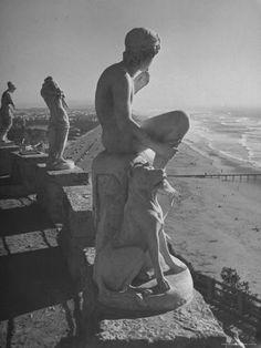 an old black and white photo of some statues on the side of a road near the beach