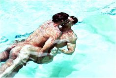 a man swimming in the water with his back turned to the camera while holding onto another man's leg