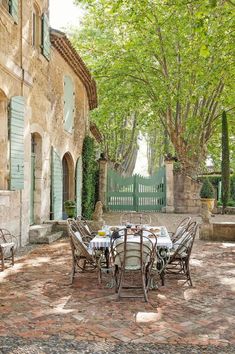 an outdoor dining table and chairs in front of a stone building with green shutters