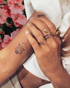 a woman's hand with two rings on her left wrist, and a cat tattoo on her right arm