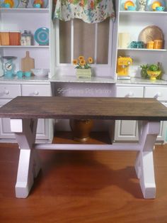 a doll house kitchen with wooden table and white cabinets